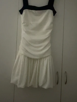 Vit och svart klänning Gina Tricot  - Supersöt kort klänning från Gina Tricot i vit med svarta breda axelband och svart kant. Använd 1 gång men inga tecken på användning och inga andra defekter. Har en balong kjol med som ett stretchigt band vid kjolen så den sitter och inte kan blåsa upp men syns inte och klänningen är väldigt stretchig. 