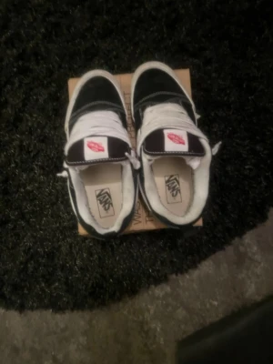 Svarta och vita Vans Old Skool sneakers - Klassiska Vans Old Skool sneakers i svart och vitt med vit sula och vita skosnören. Skorna har den ikoniska sidostripen och Vans-logga på plösen. Ovandelen är i mocka och canvas för en tidlös streetstil.