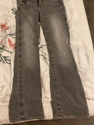 Grå bootcut jeans med fickdetalj - Säljer ett par grå bootcut jeans med snygg tvätt och ficka med knapp bak. Jeansen har klassisk femficksdesign och är tillverkade i denim med lätt stretch. Perfekta för en avslappnad och trendig look i storlek 164z