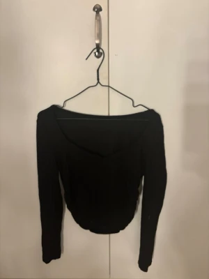 Svart croppad långärmad topp - Säljer en svart croppad topp med lång ärm och v-ringad hals. Toppen har en slim passform och är perfekt för dig som gillar en enkel men snygg stil. Materialet känns mjukt och stretchigt, troligen bomull eller polyester.