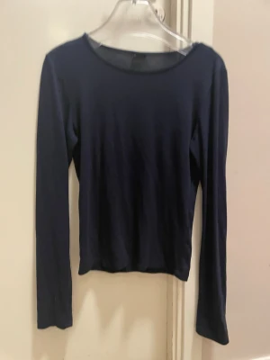 Mörkblå långärmad topp - En enkel och stilren mörkblå långärmad topp med rund halsringning. Passar perfekt till jeans eller kjol och har en smal passform som framhäver siluetten. Tillverkad i mjukt material för en bekväm känsla hela dagen.