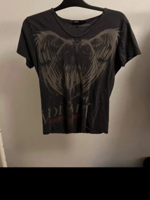 Svart Volbeat t-shirt med tryck - Cool svart t-shirt från Volbeat med stort grafiskt tryck framtill i grått och rött. T-shirten har rund halsringning och korta ärmar. Perfekt för dig som gillar bandmerch och vill ha en avslappnad stil.