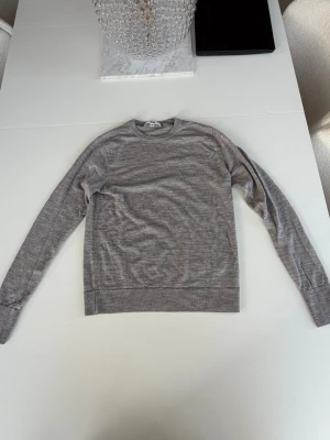 Grå stickad tröja från Uniqlo - Snygg grå stickad tröja från Uniqlo i tunn och mjuk kvalitet. Tröjan har rund halsringning, långa ärmar och ribbade muddar vid ärmslut och nederkant. Perfekt basplagg för lager på lager och enkel att matcha.