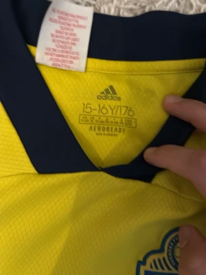 Svensk landslagströja Adidas gul - Gul svensk landslagströja från Adidas med blå detaljer och AEROREADY-material. Tröjan har V-ringning, blå Adidas-logga på bröstet och Sveriges landslagsemblem. Perfekt för fotbollsträning eller att heja på Sverige.