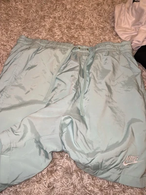 Ljusblå Nike shorts med snörning - Snygga ljusblå shorts från Nike med elastisk midja och snörning. Tillverkade i ett lätt syntetmaterial som passar perfekt för varma dagar. Nike-logga broderad på benet och praktiska sidofickor.