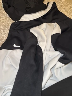 Nike svart och grå vindjacka M - Nike vindjacka i svart och grått med klassisk vit logga på bröstet. Jackan har hög krage och är tillverkad i ett lätt, syntetiskt material som passar perfekt för blåsiga dagar. Snygg sportig look och normal passform.