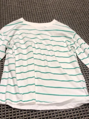 Vit och grönrandig topp från Kappahl - Vit långärmad topp från Kappahl med tunna gröna ränder. Klassisk rak passform och rund halsringning. Perfekt till jeans eller kjol för en enkel och fräsch look.