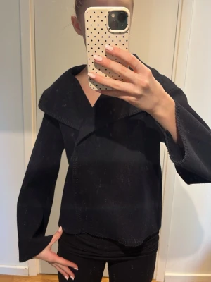 Svart kavaj med bred krage - Stilren svart kavaj med bred, markerad krage och lång ärm. Jackan har en rak passform och är tillverkad i ett mjukt material som ger en snygg siluett. Perfekt att slänga över en outfit för en clean look.