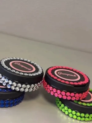 Gumpack fodral med strass - Snygga runda Gumpack snusdosor dekorerade med färgglada strasstenar i blått, silver, rosa och grönt. Perfekt för att förvara snus på ett klass sätt. Fodralen är gjorda av plast och har en trendig design som sticker ut. Dosorna är tomma och helt oanvända och nya.!
