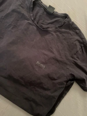 Svart kortärmad t-shirt från BOSS - En stilren svart t-shirt från BOSS med diskret logga på bröstet. Klassisk rund halsringning och korta ärmar. Perfekt basplagg för en clean och enkel look och den är storlek L passar både bra för män och kvinnor 