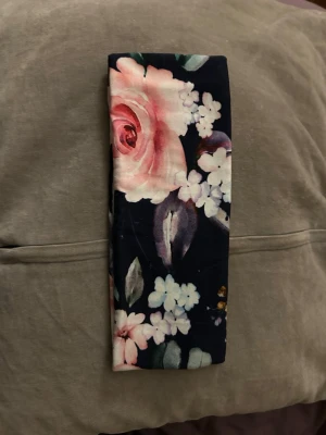 Blommigt hårband i mörkblått - Snyggt hårband med mörkblå botten och stora blommor i rosa, vitt och lila. Mjuk och stretchig känsla, perfekt för att hålla håret på plats. Passar till dig som gillar romantiska och färgglada accessoarer.