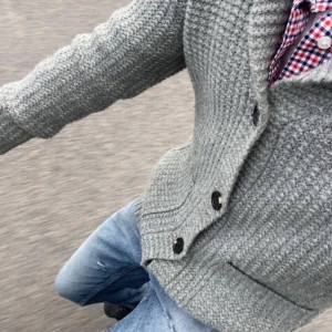 Grå Cardigan - Säljer en grå stickad kofta med krage och stora knappar framtill. Storlek L men passar M. Skitsnygg med en skjorta under! Perfekt för lager-på-lager och chill vårstil. Har du en fråga? Hör av dig! 