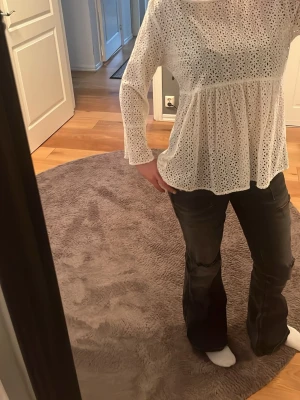 Vit broderad blus från Lindex - Söt vit blus från Lindex med broderade hålmönster och lätt utsvängda ärmar. Blusen har en lös passform och är tillverkad i ett tunt, luftigt material som ger en romantisk känsla. Perfekt att styla med jeans eller kjol.