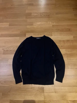 Svart stickad tröja från Dressman - Klassisk svart stickad tröja med rund halsringning och långa ärmar. Tröjan har en enkel och stilren design, perfekt att matcha med olika outfits. Materialet känns mjukt och följsamt mot huden.