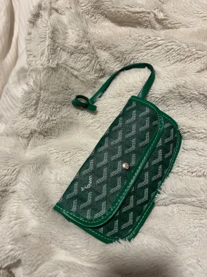 Grön plånbok med mönster - Oanvänd satt på min handväska så går att sätta fast på nycklar, väskor mm. I nyskick💚