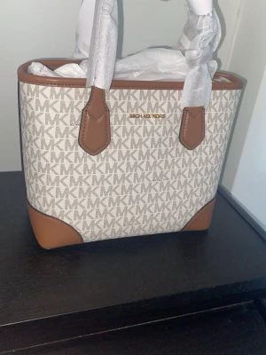 Michael Kors handväska - Säljer en helt ny Michael Kors mini-handväska i en vacker beige färg. Fick som present nyss.                                                                                        - Originalpriset är 3600 kr men köptes med rabatt. - Mått: 22L x 10B x 20H cm