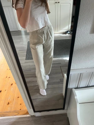 Beiga vida linnebyxor - Säljer ett par beiga linnebyxor med hög midja och vida ben. Byxorna har fickor fram och dekorativa knappar bak. Tillverkade i 100% linne.
