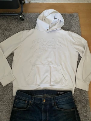 Vit hoodie från Polo Ralph Lauren - Snygg vit hoodie från Polo Ralph Lauren med broderad logga på bröstet. Klassisk känguruficka framtill och ribbade muddar vid ärmar och nederkant. Tillverkad i mjukt bomullsmaterial och har en stor huva med dragsko.
