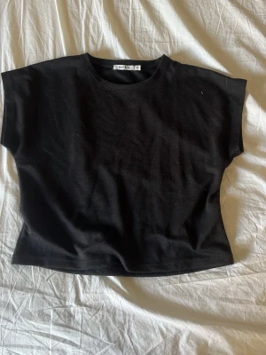 Svart kortärmad t-shirt från NA-KD - En stilren kort svart t-shirt från NA-KD med klassisk rund hals och korta ärmar. T-shirten har en rak passform och är tillverkad i mjuk bomull som känns skön mot huden. Perfekt basplagg att matcha till olika outfits. 