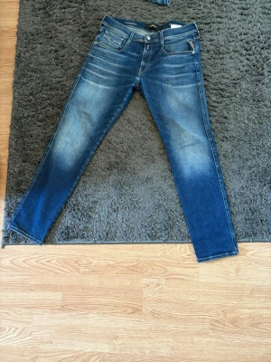 Blå slim fit jeans med slitningar från replay  - Snygga blå slim fit jeans med slitningar och tvättade detaljer på låren och knäna. Klassisk femficksmodell med dragkedja och knapp i midjan. Jeansen har kontrastsömmar och en mörkare ton nedtill på benen. Perfekta för en avslappnad och trendig look.