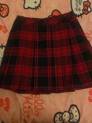 Röd och svart rutig kjol Hampton Republic - Säljer en snygg röd och svart rutig kortkjol från Hampton Republic. Kjolen har klassiskt rutmönster och A-linjeformad passform. Perfekt för dig som gillar preppy stil och vill sticka ut med ett coolt mönster.