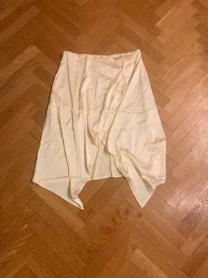 Ljusbeige omlottkjol i satin - Säljer en ljusbeige omlottkjol i satin med asymmetrisk nederkant. Kjolen har en mjuk glans och faller snyggt, perfekt för dig som gillar en unik och trendig look. Passar till många olika stilar och är enkel att matcha med både toppar och sneakers.Skriv gärna för mått! 💕