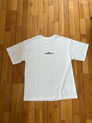 Vit margiela t-shirt med tryck - Säljer en vit t-shirt från Maison Margiela med svart texttryck på bröstet. T-shirten har klassisk passform, rund halsringning och korta ärmar. Perfekt basplagg med exklusiv känsla och diskret logga framtill.