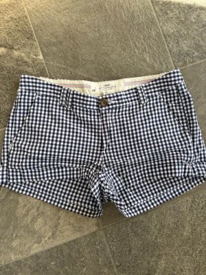 Rutiga blåvita shorts från H&M - Snygga blåvita rutiga shorts från H&M med klassiskt mönster. De har fickor fram och bak, bälteshällor och stängs med knapp och dragkedja. Perfekta för varma dagar och ger en fräsch somrig look.