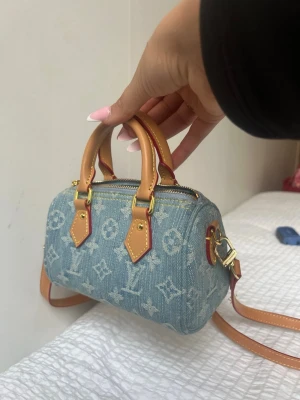 Louis Vuitton denim speedy - Trendig handväska från Louis Vuitton i blått denimtyg med klassiskt monogrammönster. Väskan har ljusbruna läderhandtag, guldfärgade metalldetaljer och dragkedja. Kommer med avtagbar axelrem för extra flexibilitet. ( 16cm )