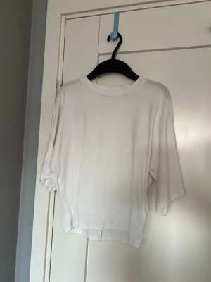 Vit loose t-shirt med vida ärmar - En enkel och stilren vit t-shirt med loose passform och vida, korta ärmar. T-shirten har rund halsringning och är tillverkad i ett mjukt material som känns skönt mot huden. Perfekt för en avslappnad look. Tröjan är tajt i midjan 