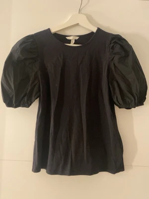 Svart topp med puffärmar från H&M - Säljer en svart topp från H&M med puffiga korta ärmar och rund halsringning. Nästan aldrig använt. Skriv om ni är intresserade. 