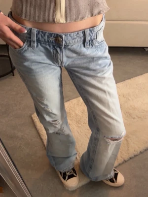 Gina tricot jeans  - Ljusblå lågmidjade jeans ifrån Gina. Jeansen har en baggy passform och flera hål samt brodyr på fickorna. Aldrig använda