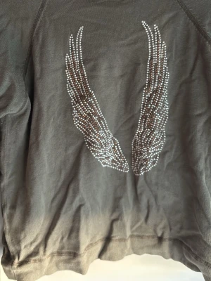 Grön topp med strassvingar - Cool grön topp med strassdetaljer på både fram- och baksidan. Baksidan har två stora vingar i strass, vilket ger en unik look. 