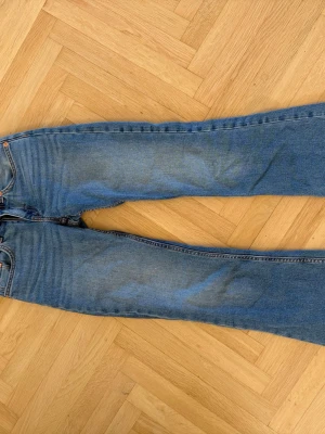 Blå bootcut jeans - Ett par klassiska blå bootcut jeans i denim med lätt slitna detaljer framtill och bakfickor. Jeansen har normal midja och dragkedja med knapp. Perfekta för en avslappnad och trendig look.