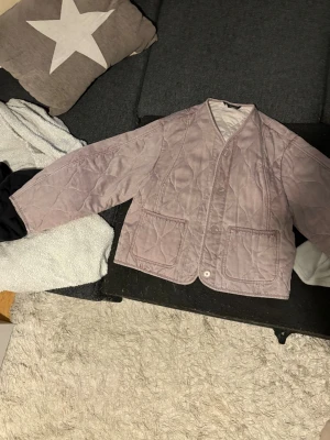 Ljuslila quiltad cardiganjacka - Quiltad cardiganjacka i ljuslila med v-ringning och knäppning framtill. Två stora fickor framtill och avslappnad passform. Jackan har ett vågigt sömmönster och är tillverkad i ett mjukt tyg som ger en trendig look. Jackan är oversized och därmed lite större passar mellan S/L beroende på hur man vill att jackan ska sitta 💓