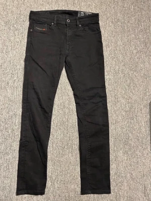Svarta slim fit jeans från Disel - Säljer ett par svarta slim fit jeans från Disel Jeans. Klassisk femficksmodell med knappgylf och diskreta sömmar. Jeansen har en smal passform och är tillverkade i mjuk bomullsdenim med lite stretch för extra komfort.