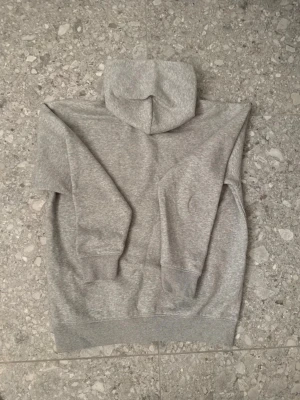 Grå hoodie från Tommy Hilfiger - Säljer en klassisk grå hoodie från Tommy Hilfiger med liten broderad logga på bröstet. Hoodien har huva, ribbade muddar vid ärmslut och nederkant samt en avslappnad passform. Tillverkad i mjukt bomullsmaterial som är perfekt för chill dagar.