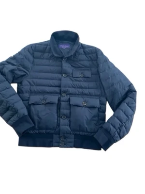 Mörkblå pufferjacka från Ralph Lauren - Snygg mörkblå pufferjacka från Ralph Lauren med quiltad design och fyra framfickor med knappar. Jackan har ribbade muddar och krage samt knappstängning framtill. Tillverkad i ett glansigt material som ger en modern look.