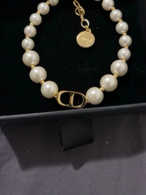 Christian Dior 30 Montaigne Pearlbracelet with gold-finish. - Elegant pärlarmband  från Dior med vita pärlor och guldfärgade detaljer. Halsbandet har en ikonisk Dior-logga i mitten och justerbar kedja med rund bricka där Dior är ingraverat. Perfekt accessoar för att lyfta din outfit. Är vintage, ca 10-15 år. Bedöms som äkta av Vestiaire Collective som har kollat igenom det o säger att det är äkta dior. 