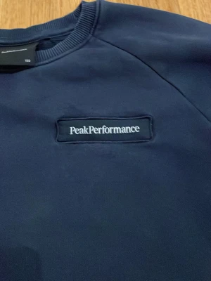 Mörkblå sweatshirt Peak Performance - Snygg mörkblå sweatshirt från Peak Performance med klassisk rund halsringning och logga broderad på bröstet. Tröjan har ribbade muddar vid ärmslut och nederkant, perfekt för en avslappnad och sportig stil.