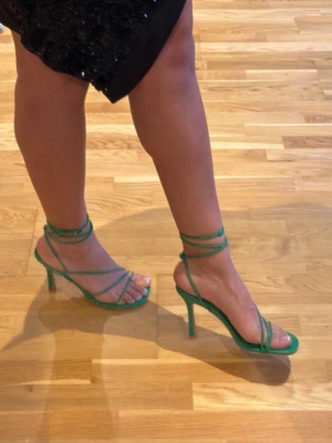 Gröna strappy pumps från NA-KD - Säljer ett par trendiga gröna pumps från NA-KD med tunna remmar och fyrkantig tå. Skorna har en perfekt klack och öppen design, perfekta för att lyfta vilken outfit som helst. Tillverkade i konstläder med stilrena detaljer. Aldrig använda 