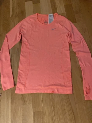Nike Dri-FIT långärmad tröja rosa helt ny utan prislapp  - Snygg långärmad tränings-tröja från Nike i en fräsch rosa färg. Tillverkad i funktionsmaterialet Dri-FIT som transporterar bort svett. Tröjan har rund halsringning, tumhål vid ärmslut och en diskret Nike-logga på bröstet. Helt ny, endast tagit bort prislapp