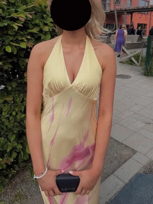 Superfin gul balklänning med rosa mönster - Säljer en lång, ljusgul halterneckklänning med rosa abstrakt mönster. Klänningen har öppen, låg rygg och knyt i nacken, samt en figurnära passform. Har bara haft den en gång på min bal och den var helt perfekt. Köpt för cirka ett år sedan i London.