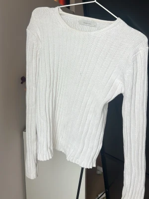 Vit ribbstickad tröja  - Klassisk vit ribbstickad tröja med rund halsringning och långa ärmar. Tröjan har en enkel, stilren design och är tillverkad i ett mjukt stickat material som passar perfekt till många olika outfits.