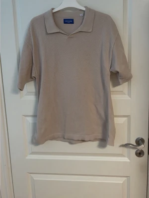 Beige piké från Jack & Jones - Klassisk beige pikétröja från Jack & Jones med krage och korta ärmar. Tillverkad i ett mjukt och strukturerat material som ger en avslappnad men ändå stilren look. Perfekt till jeans eller shorts för en enkel och snygg outfit.