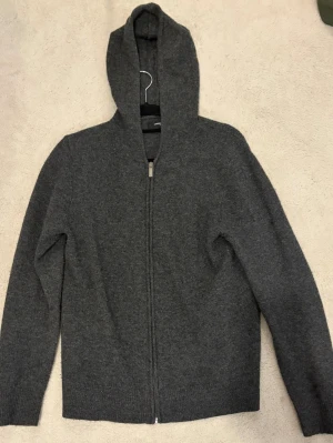 Mörkgrå hoodie i ull - Mysig mörkgrå hoodie från Lawrence Grey i mjuk ullblandning. Dragkedja framtill, huva och ribbade muddar vid ärmslut och nederkant. Perfekt för lager-på-lager och chill dagar.