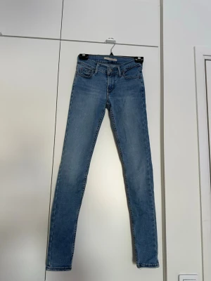 Levi's 710 Super Skinny ljusblå jeans - Säljer ett par Levi's 710 Super Skinny jeans i ljusblå denim. Modellen har hög midja, klassisk femficksdesign och smal passform hela vägen ner. Perfekta för dig som gillar en tight och stilren look. Materialet är mjukt och stretchigt för extra komfort. Jeansen har vissa slitningar som man kan se på bilderna. 