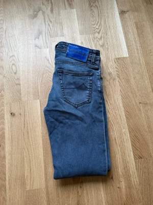Blå jeans från Jacob Cohen - Snygga blå jeans från Jacob Cohen med klassisk femficksdesign, små slitningar och en diskret logga på bakfickan. Perfekta för en stilren look. De har en dragkedja och knapp framtill.