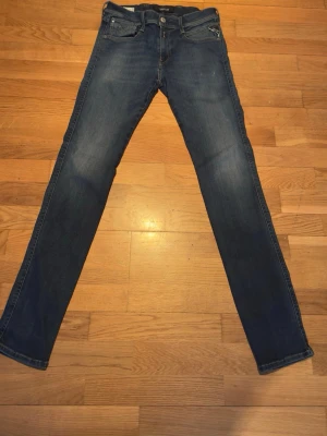 Replay anbass w30 l32 - Snygga blå slim fit jeans från Replay med klassisk femficksmodell och dragkedja. Jeansen har en lätt tvättad look och subtila slitningar för en trendig känsla. Perfekta för dig som gillar en smal passform och stilren design.
