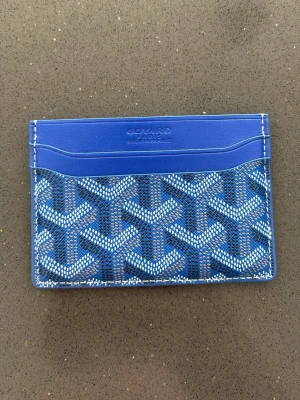Blå kortfodral i läder - Snyggt blått kortfodral med klassiskt mönster och flera fack för kort. Tillverkat i läder med Goyards ikoniska print och präglad logotyp upptill. Perfekt för att hålla ordning på dina kort och ID.